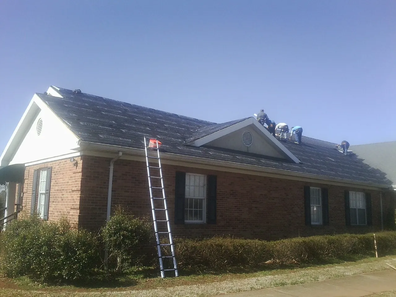 Crew tearing shingles off a brick ranch roof with a ladder set — Metal Roof Repair work by our crew in Attica